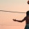 A guy jumping up to spike a volleyball in the sunset